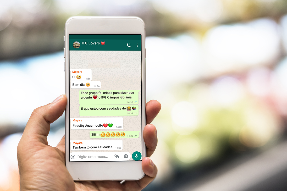 Imagem de uma pessoa segurando celular. Na tela uma conversa de whatsapp com mensagens usando emojis